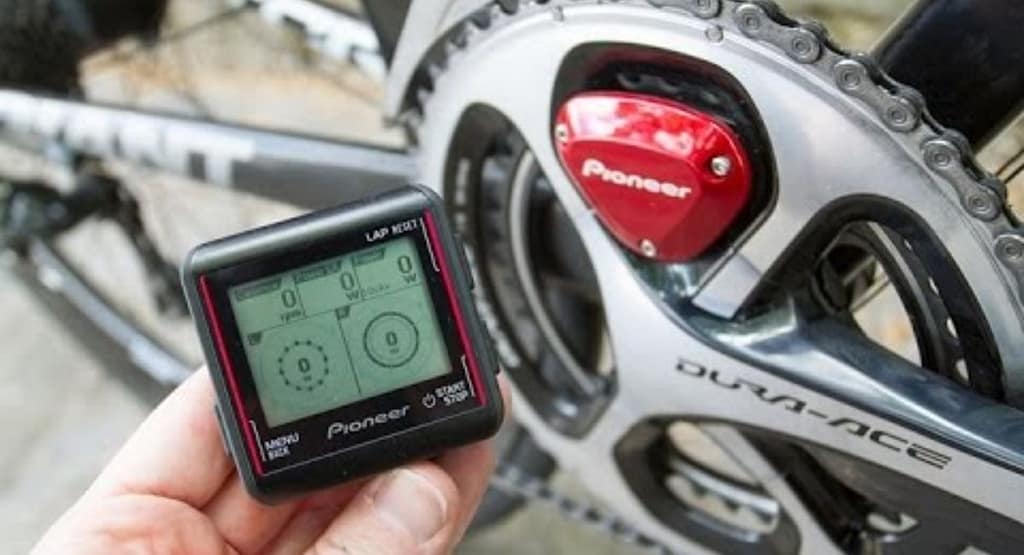 A determined cyclist rides uphill on a scenic mountain road, promoting the concept of meters power in cycling. The bold text 'INCREASE YOUR POWER' emphasizes the importance of measuring and improving cycling performance through power meters.