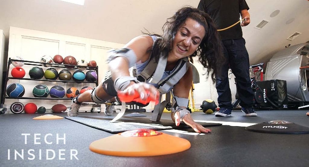 An athlete using cutting-edge sports technology during training. The scene features wearable sensors tracking biometric data, a virtual reality headset simulating game scenarios, and a smart treadmill displaying real-time performance analytics on an adjacent screen. A coach is seen analyzing data on a tablet, highlighting the role of technology in optimizing athletic performance." Let me know if you'd like adjustments or have a specific image style in mind!