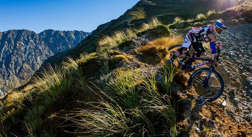 "United Cycling race competitors sprint toward the finish line, with the leading cyclist in a yellow 'LEADER' jersey raising his arm in victory. The pack of riders follows closely behind on a winding road with patches of snow in the background, showcasing the intensity of the competition."