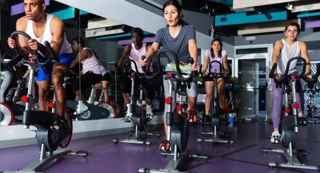 "United Cycling race competitors sprint toward the finish line, with the leading cyclist in a yellow 'LEADER' jersey raising his arm in victory. The pack of riders follows closely behind on a winding road with patches of snow in the background, showcasing the intensity of the competition."