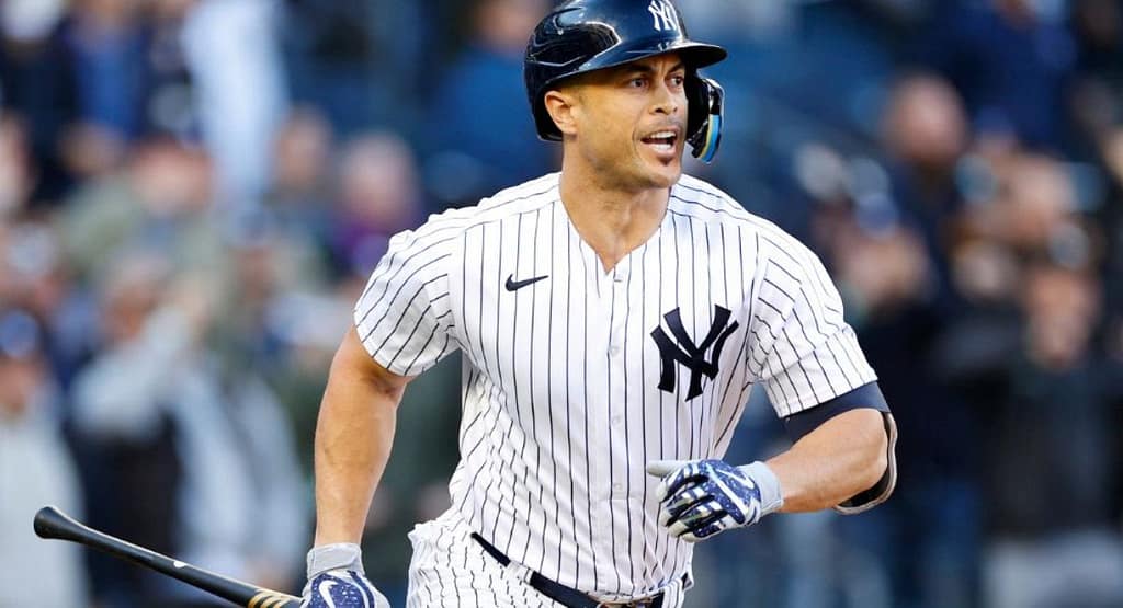 A baseball player mid-pitch on the mound, wearing a black baseball cap paired with a blue and black jersey, white pants, and cleats. The cap complements the player's athletic look while providing functional sun protection, highlighting its dual role as a style and performance essential for 2025.