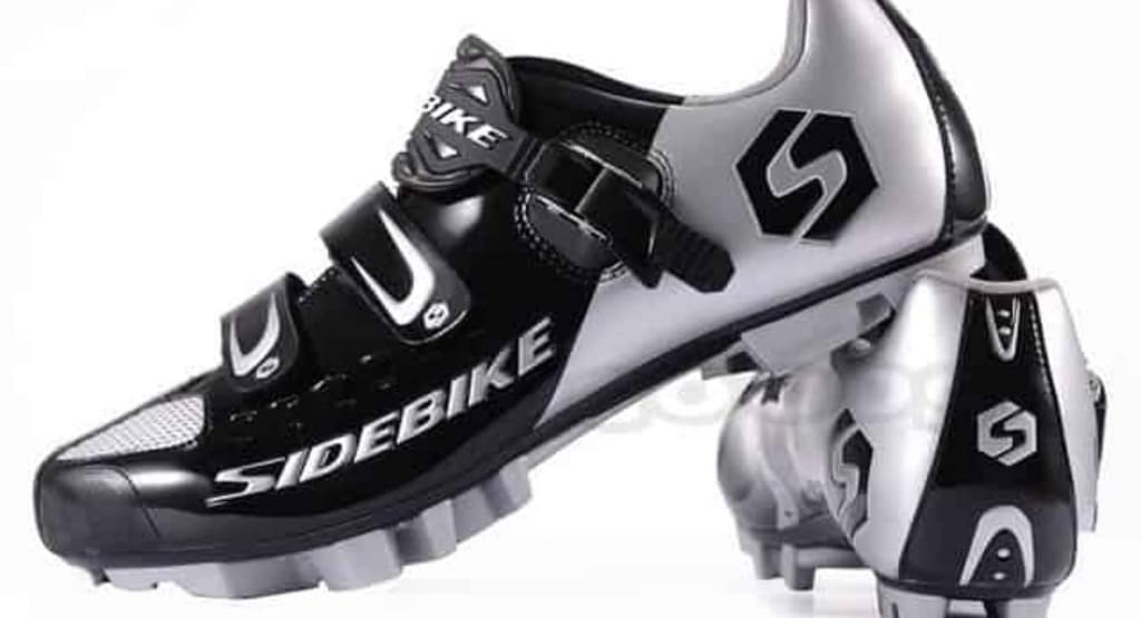 A close-up of a cyclist's foot wearing high-performance white cycling shoes with dial fasteners, clipped into the pedal of a road bike. The background features a blurred bicycle wheel and a sunlit outdoor setting, emphasizing the sport of cycling and professional gear."
Let me know if you'd like any modifications!