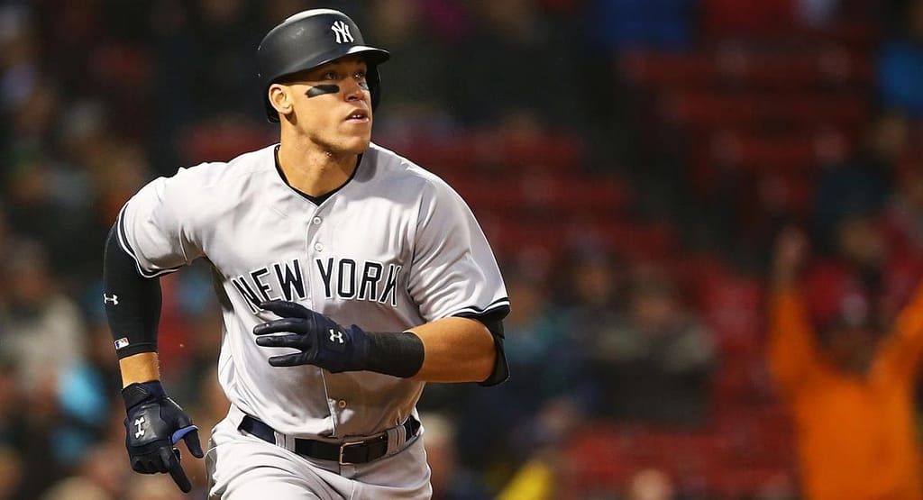 A baseball player mid-pitch on the mound, wearing a black baseball cap paired with a blue and black jersey, white pants, and cleats. The cap complements the player's athletic look while providing functional sun protection, highlighting its dual role as a style and performance essential for 2025.