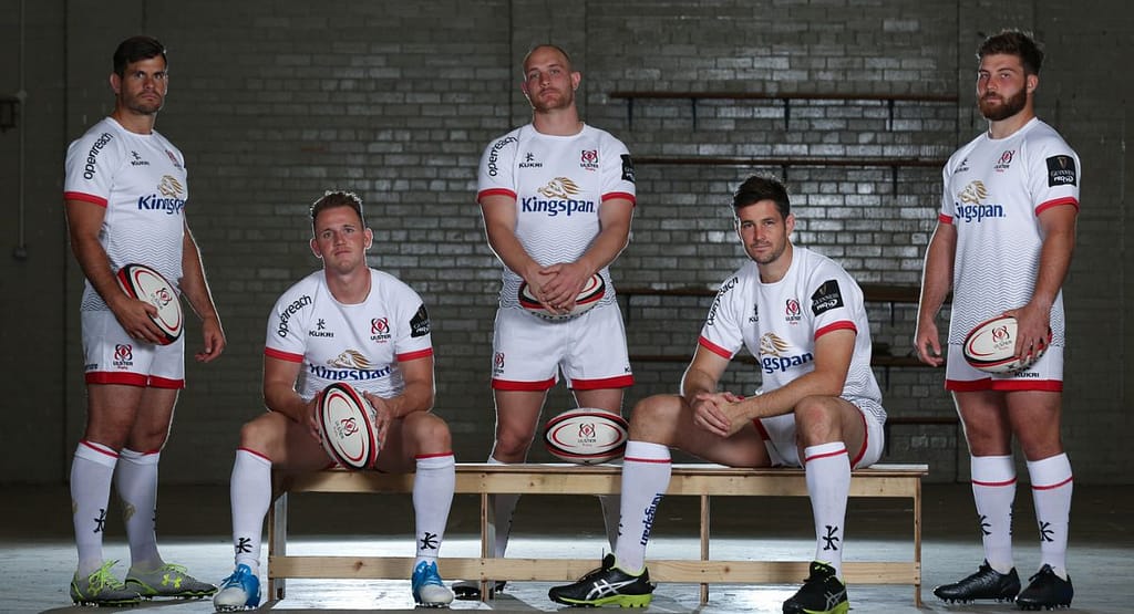 "Four male rugby players wearing professional rugby uniforms, including Akuma high-performance rugby shorts, standing confidently in a studio setting. The players are dressed in matching blue and red kits branded with 'RaboDirect' and 'BLK,' showcasing athletic fit, modern design, and functional sportswear tailored for competitive performance."