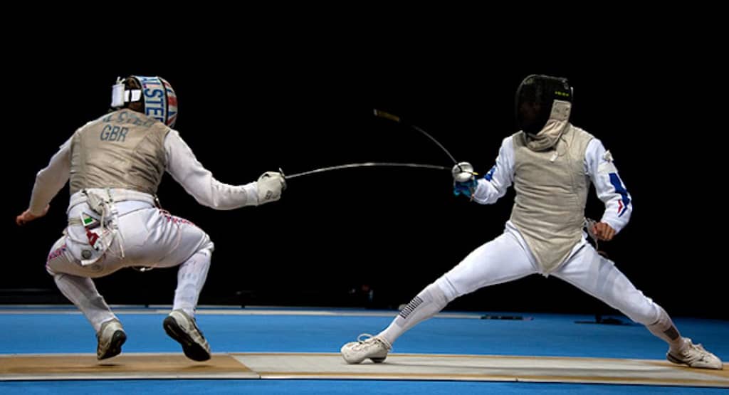 "Two fencers in mid-action during a high-speed bout, each demonstrating precise timing and explosive movement. One fencer lunges forward while the other parries with agile footwork and blade control showcasing the critical role of tempo and timing in competitive fencing."