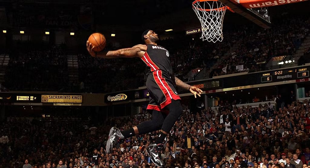 A MetroWest Basketball player in a white jersey (#9) dribbles past defenders during a high-energy game, capturing the spirit of competition and the pathways to get involved and excel in MetroWest Basketball.