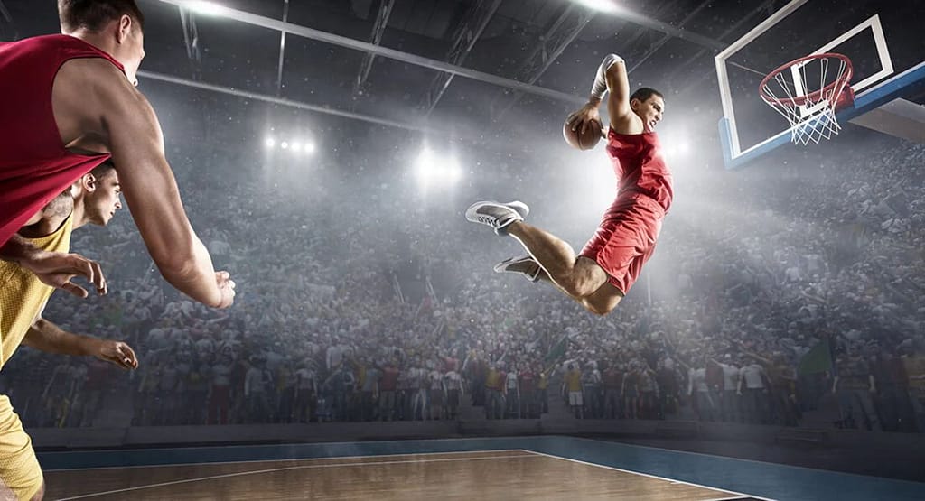 "Basketball player in a white jersey dribbling past defenders during a competitive indoor game, with spectators watching from the stands representing the intensity and skill seen in MetroWest Basketball competitions."