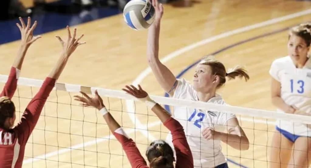 Jacqueline Opheim lunges low to dig a volleyball mid-play, showcasing intense focus, agility, and defensive skill on a professional indoor court.