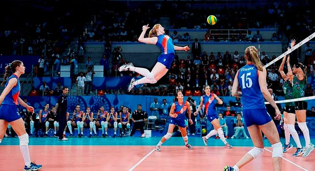 Jacqueline Opheim lunges low to dig a volleyball mid-play, showcasing intense focus, agility, and defensive skill on a professional indoor court.