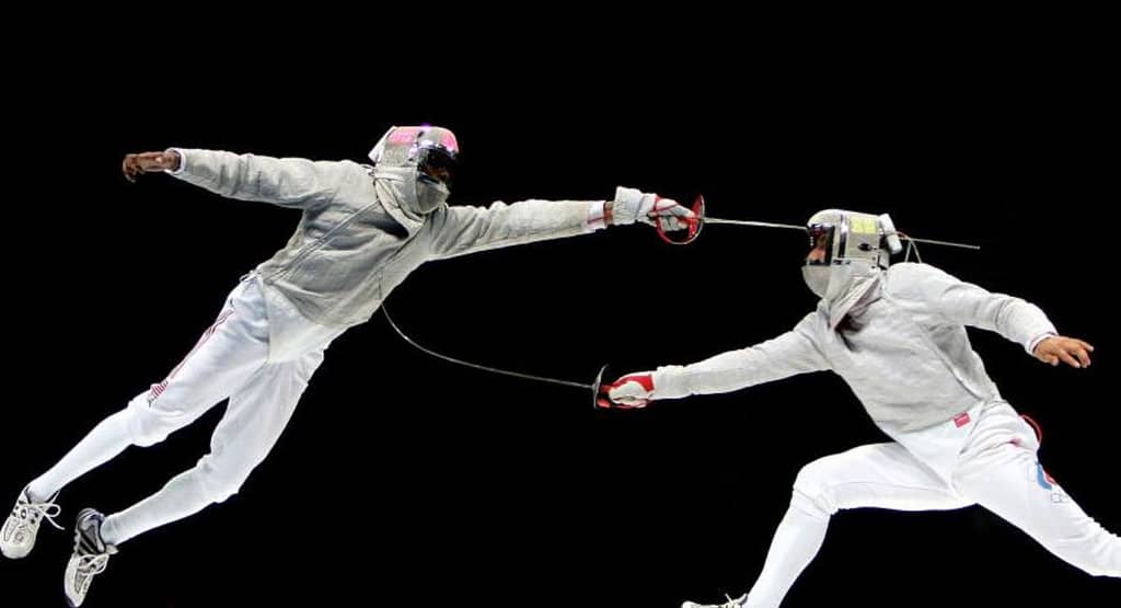 "Two fencers in mid-action during a high-speed bout, each demonstrating precise timing and explosive movement. One fencer lunges forward while the other parries with agile footwork and blade control showcasing the critical role of tempo and timing in competitive fencing."