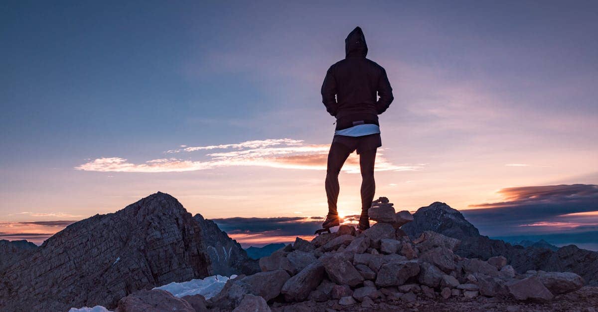 Person standing on a rocky mountain peak at sunset in Tolmin, Slovenia, embracing nature's beauty.