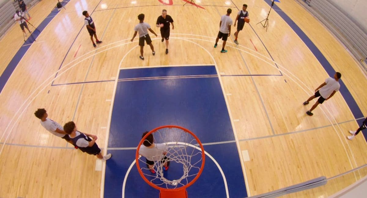 A high-angle view of basketball players practicing on an indoor court, focusing on shot techniques and positioning near the hoop. The image highlights the concept of what is field goals in basketball, emphasizing how shot efficiency plays a crucial role in modern gameplay strategies. Players are spaced out across the court, reflecting drills aimed at improving field goal percentage and overall scoring accuracy.