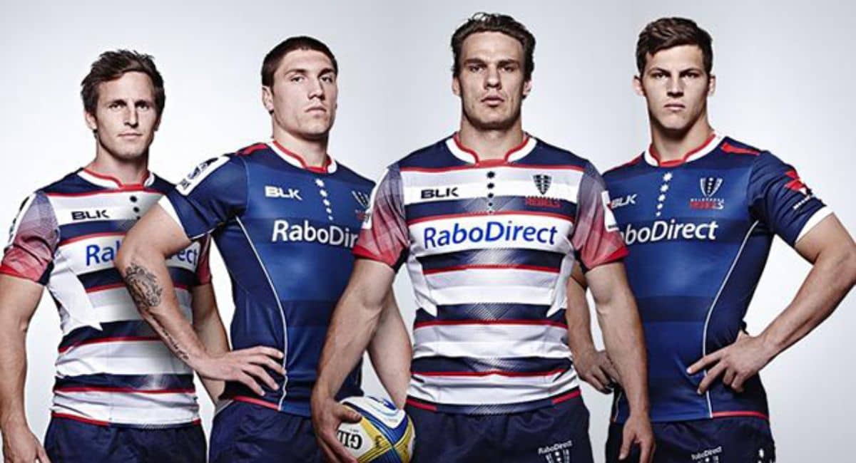"Four male rugby players wearing professional rugby uniforms, including Akuma high-performance rugby shorts, standing confidently in a studio setting. The players are dressed in matching blue and red kits branded with 'RaboDirect' and 'BLK,' showcasing athletic fit, modern design, and functional sportswear tailored for competitive performance."