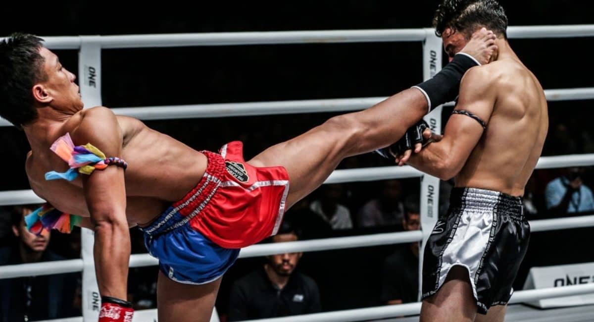 Muay Thai fighter wearing traditional Pra Jiad armbands delivers a head-level kick during a professional bout, illustrating core techniques and ranking traditions featured in Belts Muay Thai: Your Complete Guide to Ranking, Training, and Mastery.