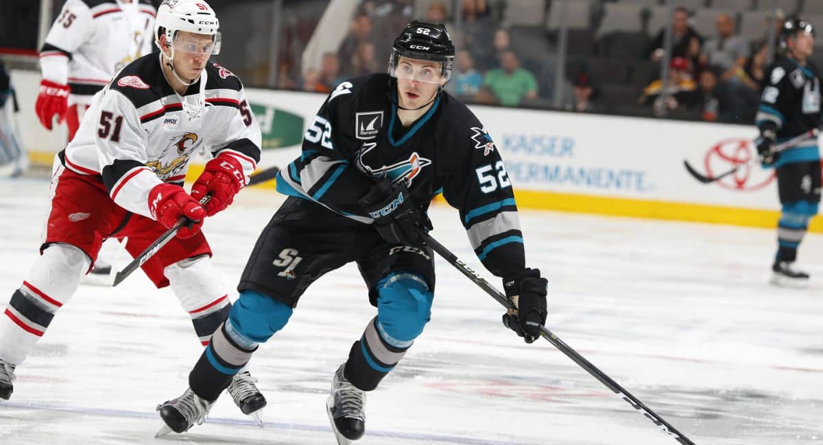 Action shot from a professional ice hockey game showing players in motion. While the image features teams in black and white/red jerseys, it does not depict the classic Chiefs hockey jersey made famous by the fictional Charlestown Chiefs from Slap Shot. The Chiefs jersey typically features blue and gold striping with bold "Chiefs" lettering across the chest