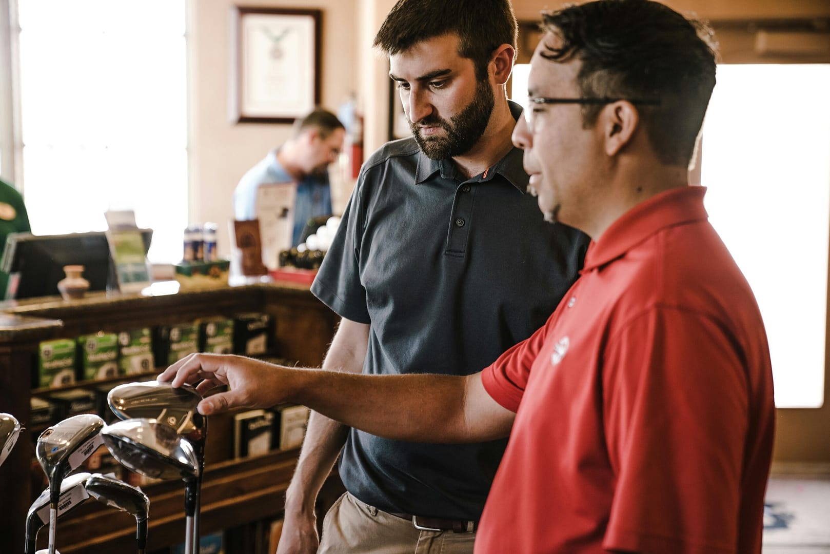 Two men in a golf store selecting golf clubs with a focus on customer service, indoors.