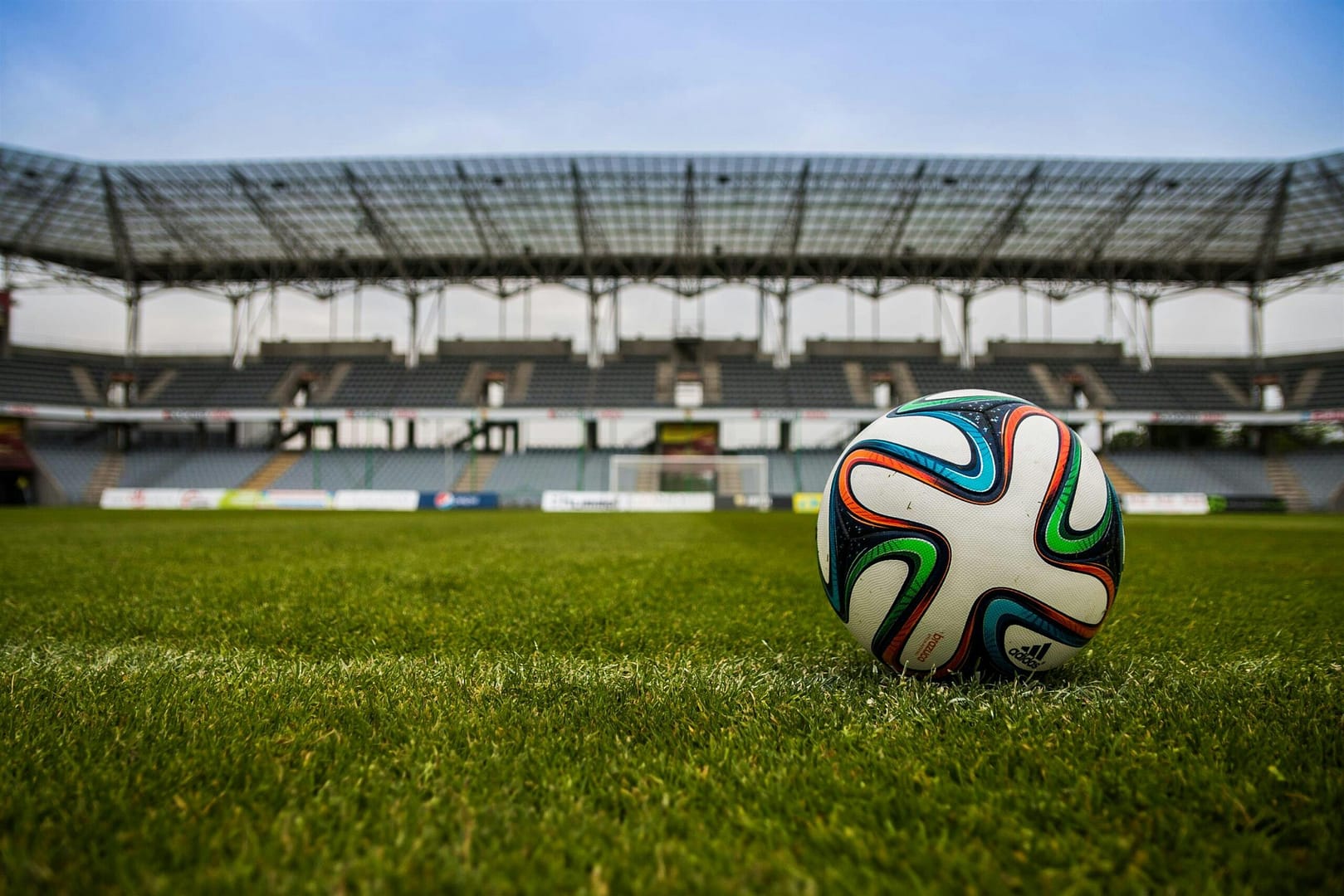 Close-up of a soccer ball on a lush grass field with an empty stadium in the background.