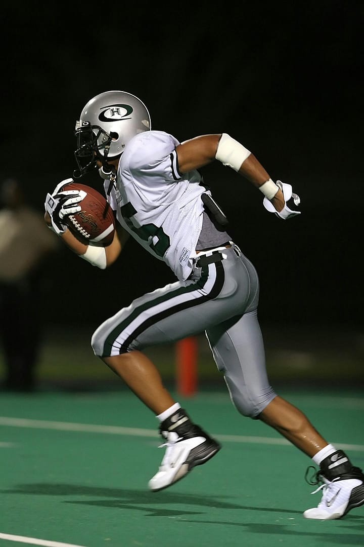 High-speed capture of a football player running on the field during a night game, showcasing athleticism.